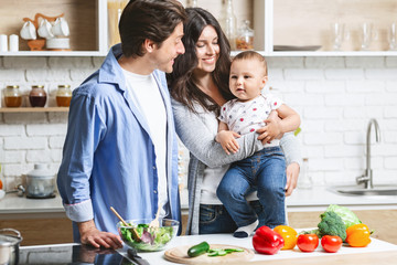 Cute baby preparing lunch with parents on kitchen table