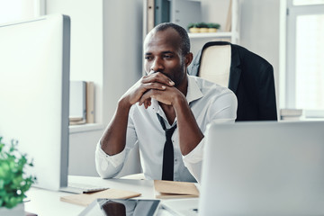 Thoughtful young African man in formalwear looking straight while working in the office