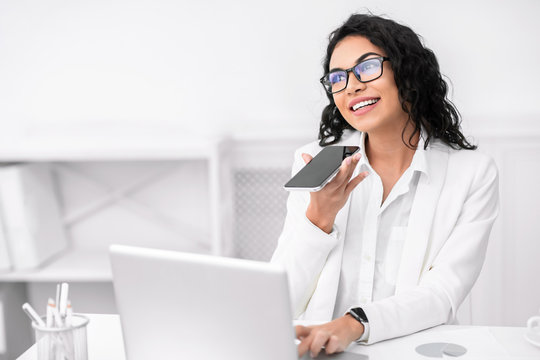 Pensive mexican woman using voice assistant on cellphone