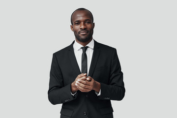 Handsome young African man in formalwear looking at camera and smiling while standing against grey background