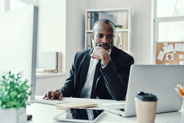 Concentrated young African man in formalwear using modern technologies while working in the office