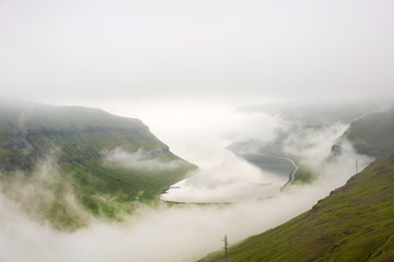 Obraz premium Incredible picture of weather on Faroe Islands in summer with thick fog around a fjord.
