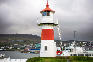 Torshavn harbor with old lighthouse on foreground, boats and overcast sky.