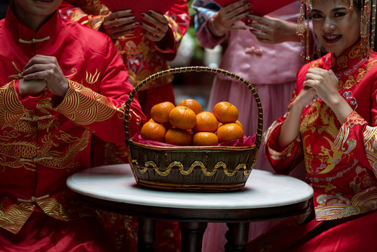 Asian woman and man in red traditional chiness dress sit at rest room,oranges basket at side,feel happy and hope in happy chinese new year