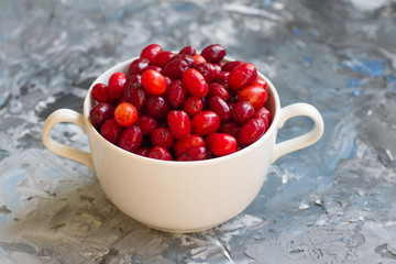 Dogwood is a sweet and sour red fruit. medicinal plant. ripe berries vitamin. Dogwood on a wooden blue background in a white plate with space for text. The concept of a healthy lifestyle