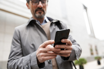 Image of serious adult businessman using cellphone while standing