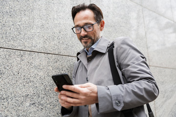 Image of joyful adult businessman using cellphone and smiling