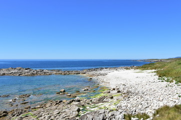 Beach with white rocks, grass and blue sky. Galicia, Spain.