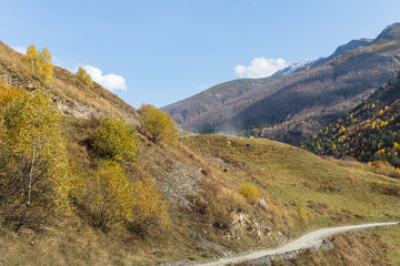 Fototapeta na wymiar The mountain road runs next to a small village located in a valley between the mountains in Svaneti in the mountainous part of Georgia