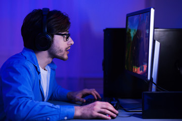 Concentrated guy playing shooter game, wearing headphones