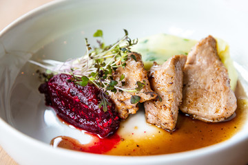 Delicious roasted pork filet cooked with smashed potatoes and smashed beetroots served in white plate.