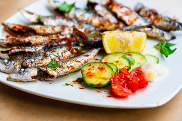 Fresh Grilled sardines served with fresh tomatoes, cucumbers slices and lemon on white plate for mediterranean healthy meal
