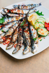 Fresh Grilled sardines served with fresh tomatoes, cucumbers slices and lemon on white plate for mediterranean healthy meal