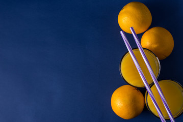  glass of fresh juice and orange on a classic trendy blue background with striped straws