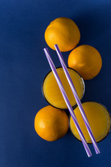  glass of fresh juice and orange on a classic trendy blue background with striped straws