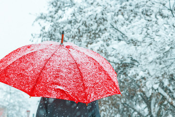 Woman under red umbrella walking in winter snow
