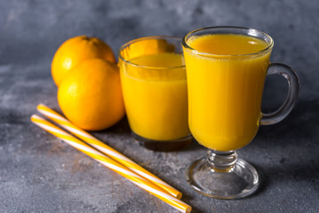  Glass of fresh orange juice, ripe orange fruits and slices on a gray stone background Freshly squeezed orange juice with a straw
