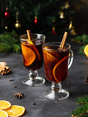 Non alcoholic Mulled wine (gluhwein) with orange slices, anise stars, spices and cinnamon sticks on dark background with spruse branches, clove and pepper. Christmas and new year card.