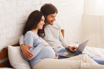 Married couple expecting baby and watching movies at home with laptop