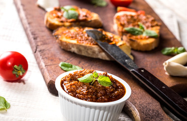 Sliced traditional toast bread with tomato pesto and basil on a cutting board and white table
