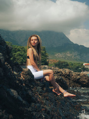 Obraz premium Young woman with dreadlocks sitting on the rocks 
