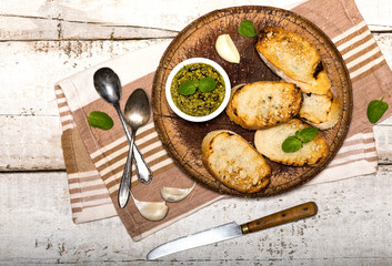 Sliced traditional toast bread with pesto and basil on a cutting board and white table