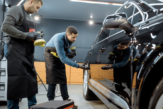 Car service workers examining glossy vehicle body coating for scratches after the polishing procedure at the service station. Car detailing concept