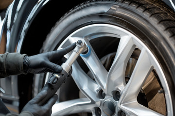 Worker in protective gloves polishing vehicle disc with professional grinder and wax from scratches, close-up