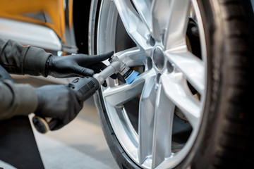 Worker in protective gloves polishing vehicle disc with professional grinder and wax from scratches, close-up