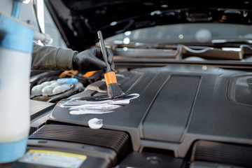 Man performs a professional car cleaning, washing engine with brush and detergent at the service station, close-up view