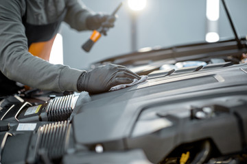 Man performs a professional car cleaning, wiping engine with microfibre at the service station, close-up view