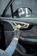 Worker provides a professional vehicle interior cleaning, wiping door panel with a brush at the car...