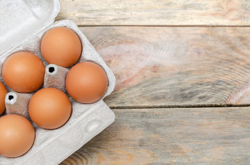 Brown chicken eggs in cardboard packaging on wooden background with copy space, view top