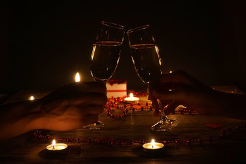 Young couple with glasses of champagne in hands close-up. Romantic candlelit dinner at the table. concept of the celebration, engagement