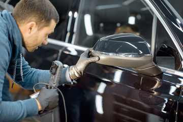 Car service worker examining vehicle body for scratches and damages, taking a car for professional...