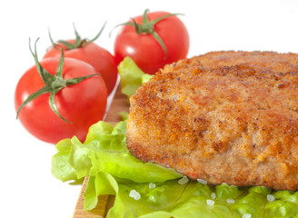 Fried meat cutlet closeup on lettuce leaves on a background of ripe cherry tomato on white background.