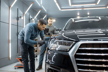 Two car service workers examining vehicle body for scratches and damages while taking a car for professional automotive detailing