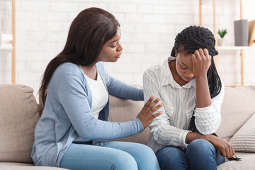 Young black woman supporting her depressed friend at home - obrazy, fototapety, plakaty