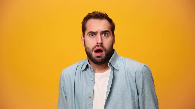 Shocked bearded young guy 20s in denim shirt white t-shirt isolated over yellow background in studio. People sincere emotions, lifestyle concept. Looking at camera with scared look, fearful glance.