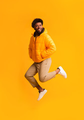 Fototapeta na wymiar Joyful afro guy in warm jacket jumping in the air
