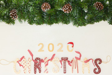 Concept: Marry Christmas and Happy New Year 2020. Beautiful Festive Vintage Garland and Christmas Tree Branches with Pine Cones are on White Wooden Background. Top View, Flat Lay Composition.