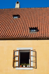 Open window with flowers on a windowsill with a tiled brown roof and chimney
