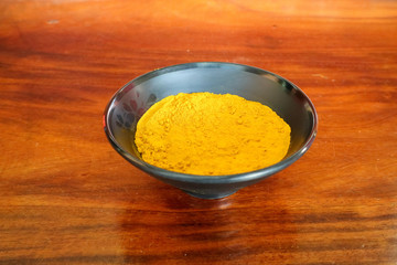 Turmeric powder in a black cup with a brown wooden floor