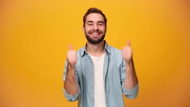 Handsome smiling guy 20s in denim shirt white t-shirt isolated on yellow background in studio. People sincere emotions, lifestyle concept. Look approvingly pointing fingers to camera showing thumbs up
