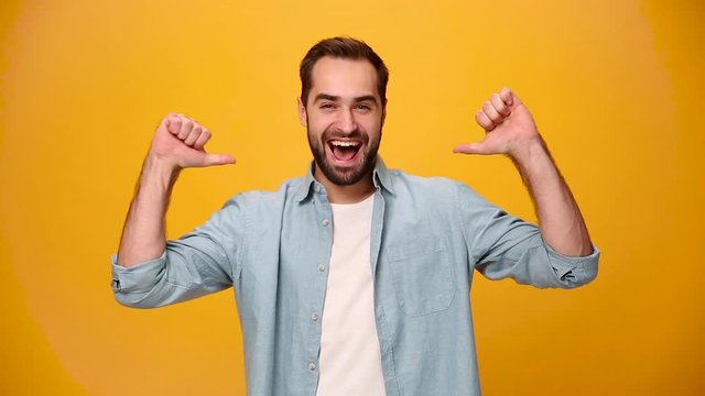 Handsome confident bearded young guy 20s in denim shirt white t-shirt isolated on yellow background in studio. People sincere emotions, lifestyle concept. Looking at camera pointing fingers on himself