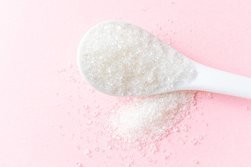 .White teaspoon with crumbly sugar on a pink background. Fly Lay, minimalism, copyspace, top view. Unhealthy sweet food concept.