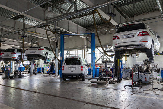 Four white used cars with an open hood raised on a lift for repairing the chassis and engine in a vehicle repair shop. Auto service industry.