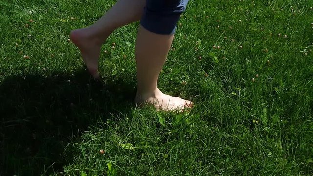 Side view of woman legs in blue tights walking slowly on barefoot on green grass in a park 