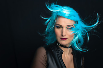 A girl on a black background with blue wig and hair in the wind