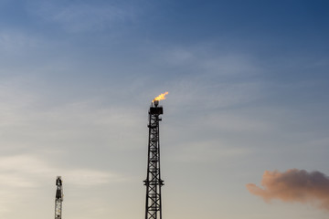 Obraz premium Oil Production flare tower and crane boom side by side during sunset at oil field
